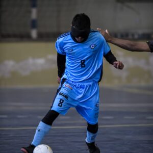 Atleta Júnior Fernandes uniformizado com a camisa número 8 do INV, conduzindo a bola numa partida de futebol de Cegos.