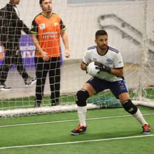 Goleiro Hyuri, com uniforme branco do INV, segurando a bola numa partida de futebol de cegos.